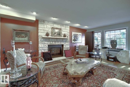 Living area featuring a stone fireplace, recessed lighting, and large windows providing natural light - 11126 52 Street, Edmonton, AB - Indoor Photo Showing Living Room With Fireplace