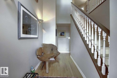 Inviting entryway featuring light wood flooring, a staircase with white balusters and a dark wood handrail, and a wall-mounted light fixture - 11126 52 Street, Edmonton, AB - Indoor Photo Showing Other Room