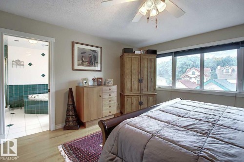 The bedroom features hardwood flooring and a ceiling fan, with a wide window providing views of the surrounding area - 11126 52 Street, Edmonton, AB - Indoor Photo Showing Bedroom