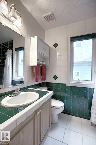 Bathroom with white floor tiles, a window, and a vanity featuring a white sink and wood-toned cabinetry - 11126 52 Street, Edmonton, AB - Indoor Photo Showing Bathroom