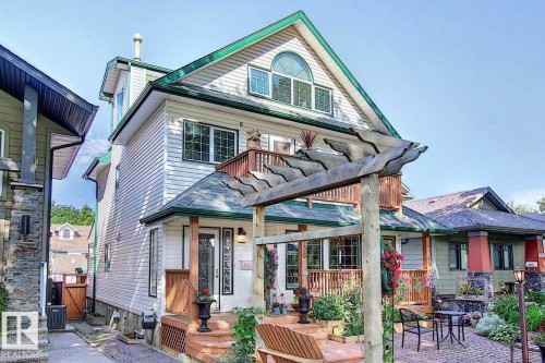 The property features white siding with green trim, a front porch with a wooden pergola, and a second-story balcony - 11126 52 Street, Edmonton, AB - Outdoor With Deck Patio Veranda