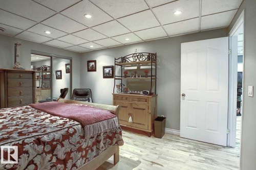 This room features a grid-patterned ceiling with recessed lighting, light-toned wood flooring, and light gray walls - 11126 52 Street, Edmonton, AB - Indoor Photo Showing Bedroom