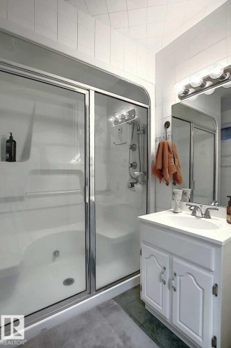 Bathroom featuring a white vanity with a single sink, a mirror with an overhead light fixture, and a shower with sliding glass doors - 11126 52 Street, Edmonton, AB - Indoor Photo Showing Bathroom