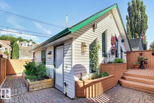 This property features a charming exterior with white siding, a green roofline, and distinctive angled windows - 11126 52 Street, Edmonton, AB - Outdoor With Deck Patio Veranda