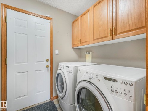 Dedicated laundry area featuring overhead wooden cabinetry, a white paneled door with brass hardware, and two front-loading appliances - 11704 11 Avenue, Edmonton, AB - Indoor Photo Showing Laundry Room