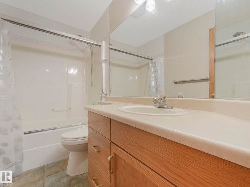 Bathroom featuring a vanity with a white countertop and an integrated sink, a large mirror, a toilet, and a bathtub with a shower and shower curtain - 11704 11 Avenue, Edmonton, AB - Indoor Photo Showing Bathroom