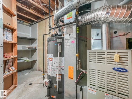 The utility area features a water heater, a Carrier furnace unit, and extensive exposed ductwork - 11704 11 Avenue, Edmonton, AB - Indoor Photo Showing Basement