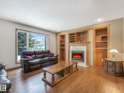 Living room featuring hardwood flooring, a large window, and an electric fireplace with a mantel and built-in shelving - 11704 11 Avenue, Edmonton, AB - Indoor Photo Showing Living Room With Fireplace