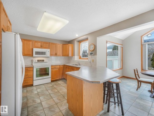 The kitchen features light wood cabinetry, white appliances, and tiled flooring - 11704 11 Avenue, Edmonton, AB - Indoor Photo Showing Kitchen With Double Sink