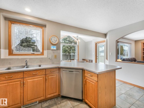 The kitchen features wooden cabinetry, a double basin sink, and a stainless steel dishwasher - 11704 11 Avenue, Edmonton, AB - Indoor Photo Showing Kitchen With Double Sink