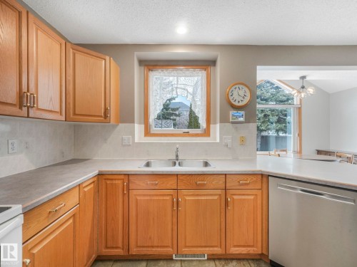 The kitchen features wood cabinetry, a double basin sink, and a stainless steel dishwasher - 11704 11 Avenue, Edmonton, AB - Indoor Photo Showing Kitchen With Double Sink