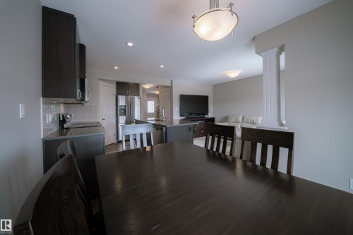 Open concept living space featuring a dining area with a dark wood table, a kitchen with dark cabinetry, stainless steel appliances, and a tiled backsplash, and a living area with light-colored walls - 2132 52 St, Edmonton, AB - Indoor Photo Showing Dining Room