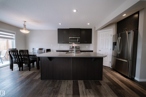 Open concept kitchen and dining area featuring dark wood flooring, dark cabinetry, light countertops, stainless steel appliances, and a sliding glass door leading to an outdoor space - 2132 52 St, Edmonton, AB - Indoor