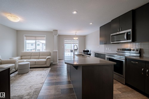Open concept living area featuring dark wood-style flooring, a kitchen with dark cabinetry, stainless steel appliances, and a light-colored countertop - 2132 52 St, Edmonton, AB - Indoor