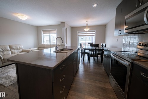 The kitchen features a spacious island with a double sink, dark cabinetry, and integrated stainless steel appliances - 2132 52 St, Edmonton, AB - Indoor Photo Showing Kitchen With Double Sink