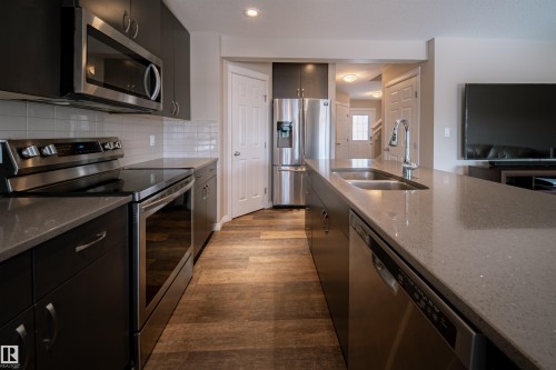 Well-appointed kitchen featuring dark cabinetry, stainless steel appliances, a white subway tile backsplash, and a large island with a double sink - 2132 52 St, Edmonton, AB - Indoor Photo Showing Kitchen With Double Sink With Upgraded Kitchen