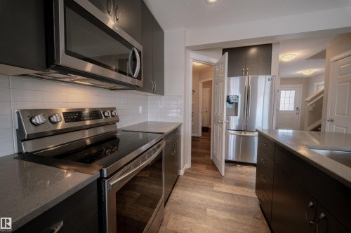 The kitchen features stainless steel appliances, dark cabinetry, light countertops, and a white subway tile backsplash - 2132 52 St, Edmonton, AB - Indoor Photo Showing Kitchen