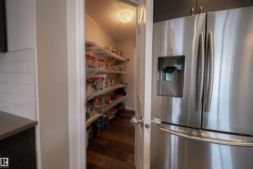 The property features a kitchen with a stainless steel refrigerator and an organized pantry with extensive shelving and wood-style flooring - 2132 52 St, Edmonton, AB - Indoor