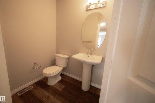 Bathroom featuring a pedestal sink, an oval mirror with an overhead light fixture, and wood-look flooring - 2132 52 St, Edmonton, AB - Indoor Photo Showing Bathroom