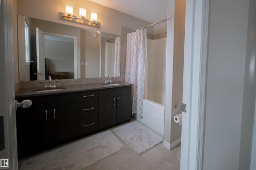The bathroom features a double vanity with dark cabinetry, dual sinks, and an expansive mirror - 2132 52 St, Edmonton, AB - Indoor Photo Showing Bathroom
