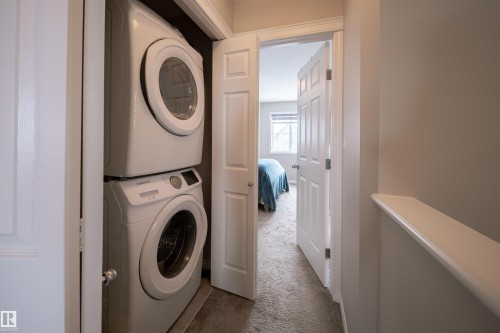 The property features a dedicated laundry area with a stacked washer and dryer, conveniently located near a carpeted room with a window - 2132 52 St, Edmonton, AB - Indoor Photo Showing Laundry Room