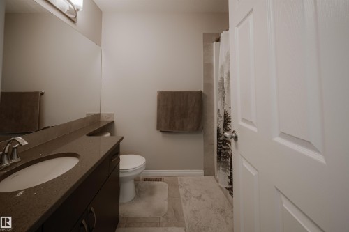 Bathroom featuring a vanity with a countertop and integrated sink, a toilet, and a shower with a patterned shower curtain - 2132 52 St, Edmonton, AB - Indoor Photo Showing Bathroom
