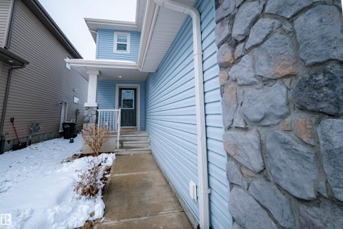 The property features light blue siding, a covered entrance with white railings, and a stone accent column - 2132 52 St, Edmonton, AB - Outdoor