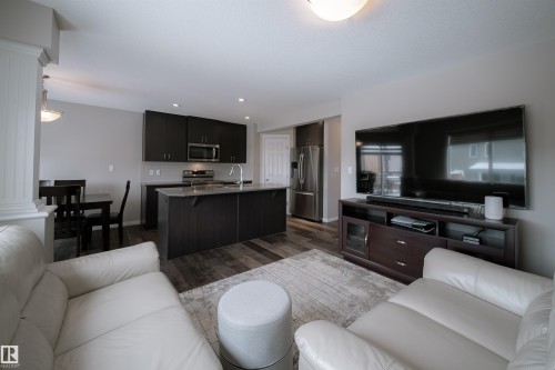 Open-concept living area with wood-look flooring, a kitchen featuring dark cabinetry and stainless steel appliances, and a dining area - 2132 52 St, Edmonton, AB - Indoor Photo Showing Living Room
