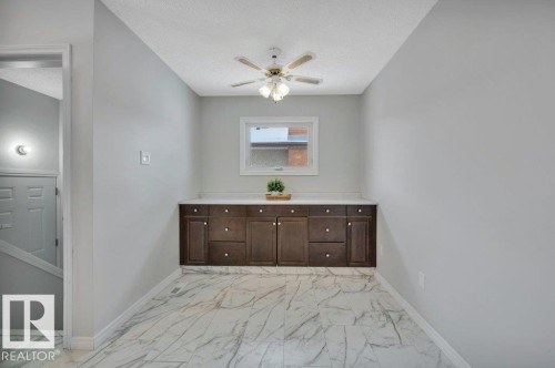 This room features a built-in cabinetry with a countertop, a window providing natural light, and a ceiling fan with integrated lighting - 12140 53 Street, Edmonton, AB - Indoor