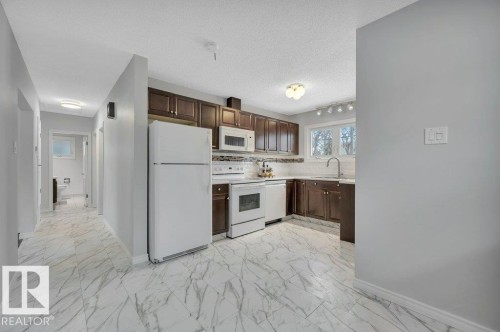 Well-appointed kitchen featuring dark wood cabinetry, white appliances, and a white tile backsplash - 12140 53 Street, Edmonton, AB - Indoor Photo Showing Kitchen