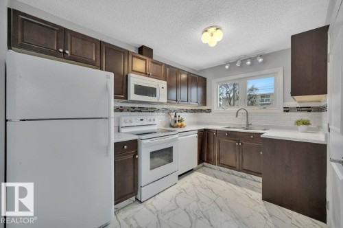 The kitchen features dark wood cabinetry, white appliances, and a white countertop - 12140 53 Street, Edmonton, AB - Indoor Photo Showing Kitchen