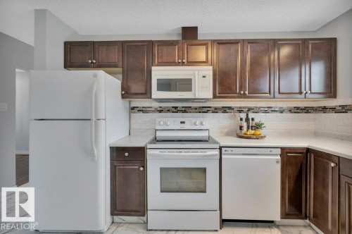 The kitchen features dark wood cabinetry, white appliances, and a subway tile backsplash with decorative accents - 12140 53 Street, Edmonton, AB - Indoor Photo Showing Kitchen