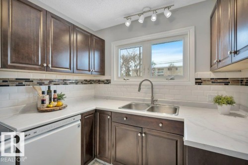 The kitchen features dark wood cabinetry, white countertops, and a subway tile backsplash with a decorative accent strip - 12140 53 Street, Edmonton, AB - Indoor Photo Showing Kitchen With Double Sink