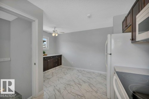 Kitchen area featuring white appliances, dark wood cabinetry, and a ceiling fan - 12140 53 Street, Edmonton, AB - Indoor