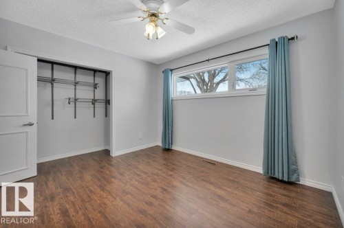 This room features rich wood flooring, a window with a view of trees, and an open closet with shelving - 12140 53 Street, Edmonton, AB - Indoor Photo Showing Other Room