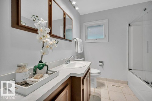 Bathroom featuring a vanity with a white countertop and a white sink, a mirror with a wooden frame, and a bathtub with a glass enclosure - 12140 53 Street, Edmonton, AB - Indoor Photo Showing Bathroom