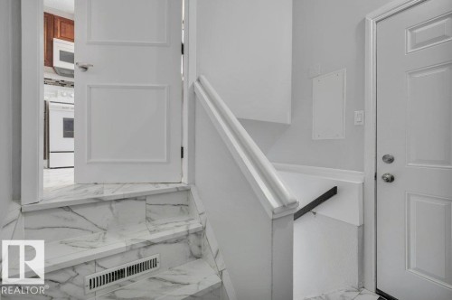 Entryway featuring white paneled doors, a white staircase with marble-patterned treads, and white walls - 12140 53 Street, Edmonton, AB - Indoor Photo Showing Other Room