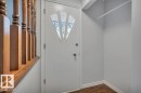 Entryway featuring a white door with decorative glass inserts, wood-toned flooring, and a wooden stair railing - 12140 53 Street, Edmonton, AB  - Indoor Photo Showing Other Room 