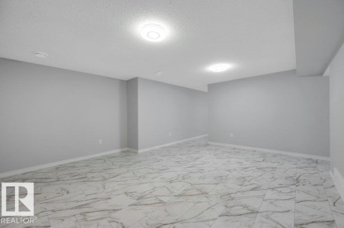 Expansive room featuring light gray walls, white baseboards, and stylish marble-patterned floor tiling - 12140 53 Street, Edmonton, AB - Indoor