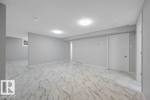 Spacious room featuring light-colored walls and white marble-style floor tiles, with recessed lighting and a window providing natural light - 12140 53 Street, Edmonton, AB - Indoor