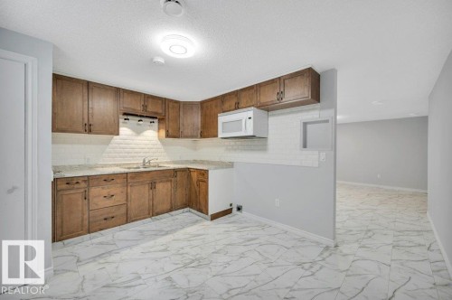 The kitchen features wood cabinetry, a white subway tile backsplash, and a built-in microwave - 12140 53 Street, Edmonton, AB - Indoor Photo Showing Kitchen