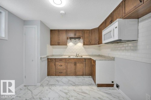 Kitchenette featuring wood cabinetry, a white subway tile backsplash, granite countertops, and a built-in microwave - 12140 53 Street, Edmonton, AB - Indoor Photo Showing Kitchen With Double Sink