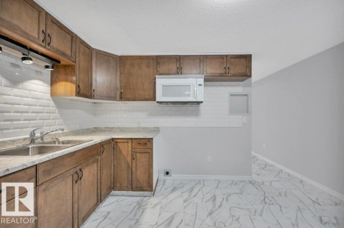 The kitchen features wooden cabinetry, a stainless steel sink with a faucet, and a subway tile backsplash - 12140 53 Street, Edmonton, AB - Indoor Photo Showing Kitchen With Double Sink