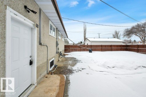 The property features a private yard enclosed by a brown fence, with a white exterior door providing direct outdoor access - 12140 53 Street, Edmonton, AB - Outdoor With Exterior
