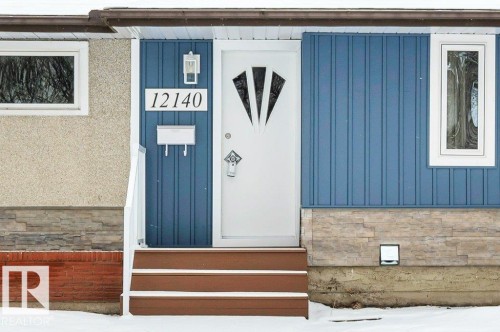The property features a white entry door with decorative glass inserts, complemented by blue vertical siding and white trim - 12140 53 Street, Edmonton, AB - Outdoor With Exterior