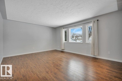 Spacious room featuring wood flooring, light grey walls, and a large window with white trim - 12140 53 Street, Edmonton, AB - Indoor Photo Showing Other Room