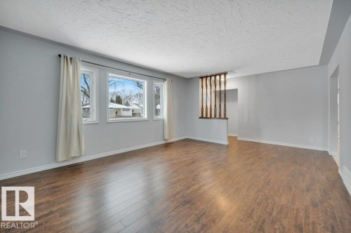 The property features a bright living space with large windows, hardwood flooring, and a decorative wooden room divider - 12140 53 Street, Edmonton, AB - Indoor Photo Showing Other Room