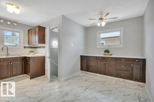 The kitchen and dining area features white tile flooring, dark wood cabinetry with white countertops, and a ceiling fan - 12140 53 Street, Edmonton, AB - Indoor Photo Showing Kitchen