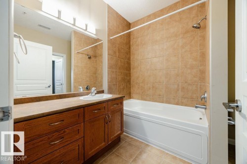 Bathroom featuring a vanity with a sink, a large mirror, and a jetted tub with tile surround - 217 160 Magrath Road, Edmonton, AB - Indoor Photo Showing Bathroom