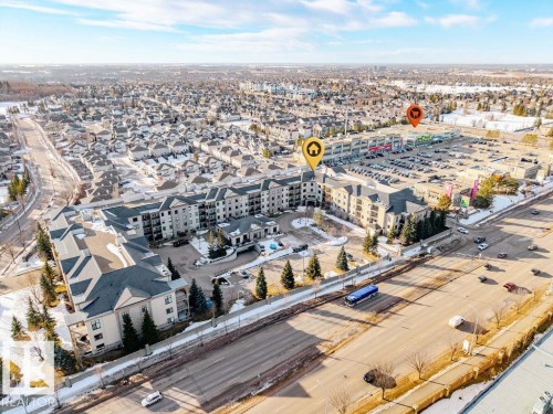 Aerial view of the property and its surrounding area, featuring a multi-story building with balconies, a paved parking lot, and nearby residential streets - 217 160 Magrath Road, Edmonton, AB - Outdoor With View